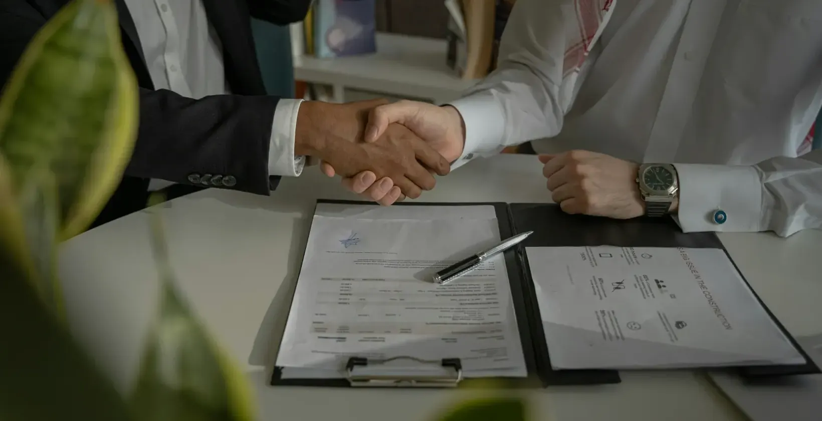 Two people shaking hands across a desk with signed documents