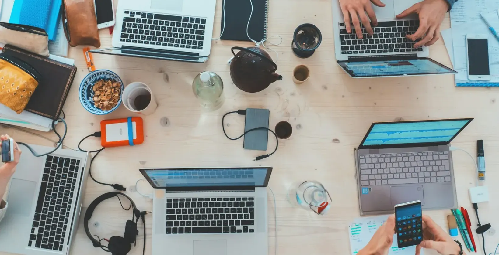 Several people working on laptops and phones at a shared desk, seen from above